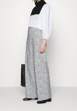 Vrouw draagt een zwart-wit coltop met pofmouwen en een wijde broek met een zwart-wit geometrisch patroon.