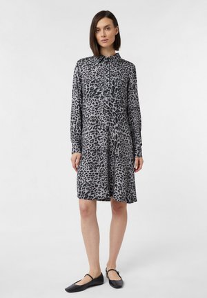 Abito grigio con stampa leopardata, maniche lunghe, colletto abbottonato e vita arricciata. Indossato con scarpe nere basse, silhouette al ginocchio.