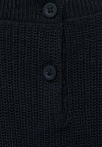 Fabbricazione di un maglione lavorato a maglia nero con un motivo testurizzato, dotato di due bottoni in plastica nera e un piccolo pannello di bottoni.