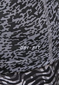 Casquette grise avec un motif abstrait noir, étiquette "DRI-FIT" en blanc, tissu texturé et surpiqûres contrastantes le long des coutures.