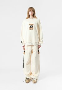 Sudadera oversized crema con un diseño de oso, combinada con pantalones crema a juego. Corte holgado, tejido suave y detalles de oso en los pantalones.