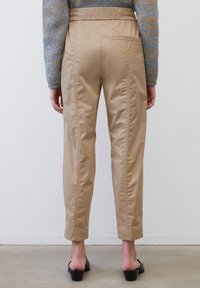 Beige, elastische broeken met een ontspannen pasvorm, voorzien van zijnaaddetails en steekzakken, gecombineerd met zwarte sandalen op blokhak.