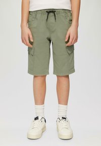 Khakifarbene Cargo-Shorts mit zwei Seitentaschen, elastischem Bund und Kordelzug. Getragen mit weißen Socken und weißen Sneakers mit navyfarbenen Akzenten.
