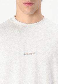 T-shirt di cotone grigio chiaro con collo rotondo, presenta il testo ricamato "LES DEUX" in un colore a contrasto sul petto.