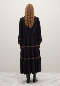 Long black dress made of lightweight fabric, featuring puffed sleeves and tiers with brown crochet detailing at the waist and sleeves.