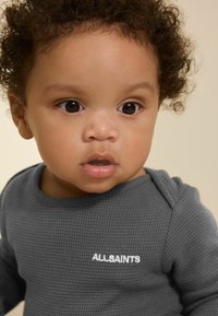 Graues Waffelstrick-langarmshirt mit rundem Ausschnitt und weißem "ALLSAINTS"-Logo auf der Brust. Glatte Stoffqualität und strukturierte Oberfläche.