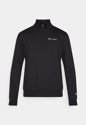 Svart genser med kvartglidelås i kragen, med liten hvit "Champion"-logo på brystet og ribbestrikkede mansjetter. Mykt, teksturert stoff.