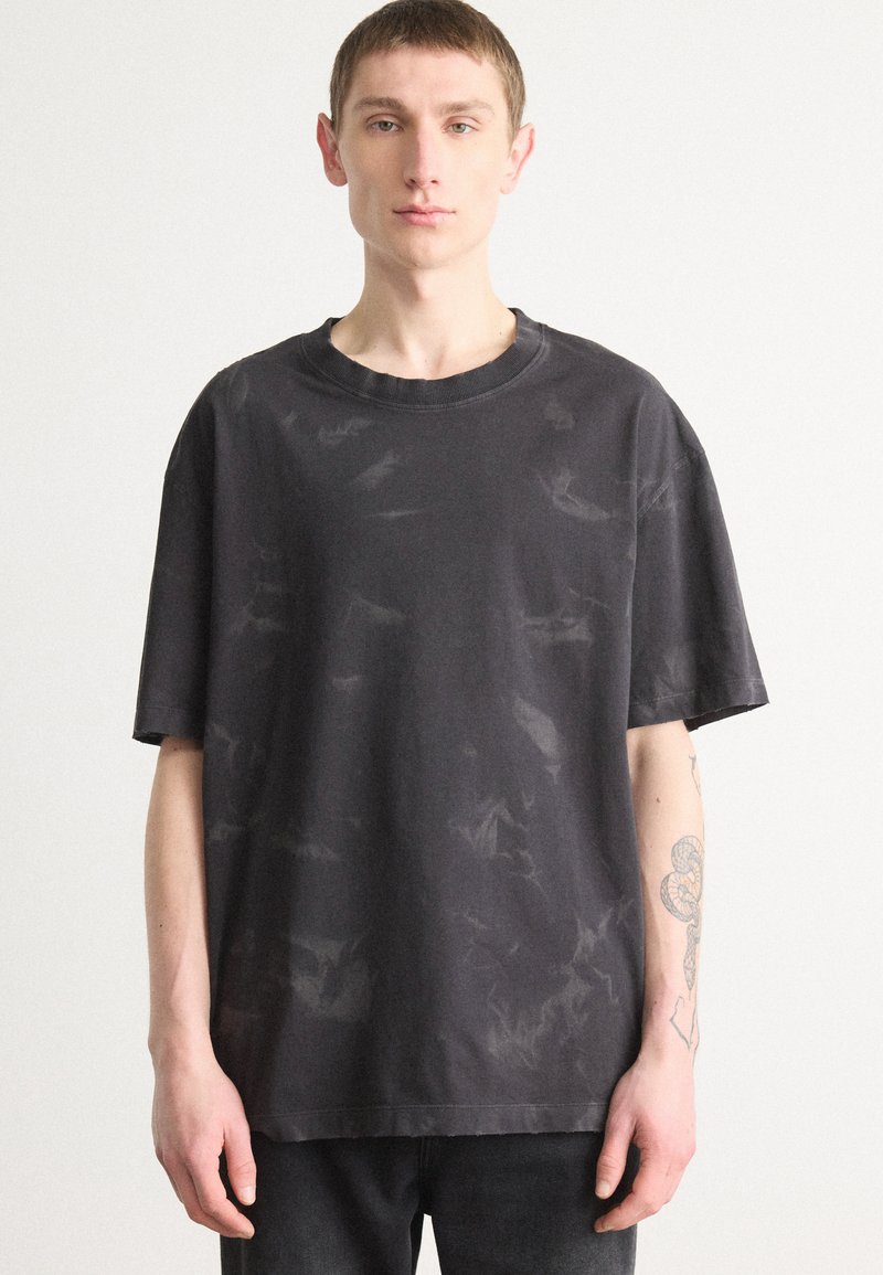 Svart bomulls oversized t-skjorte med korte ermer, med en subtil tekstur og svakt mønster. Crew-hals, avslappet passform.