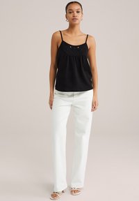Top nero senza maniche con dettagli ricamati, vestibilità rilassata e spalline sottili, abbinato a pantaloni a gamba larga di colore chiaro.