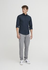 Laivaston nappikauluspaita pitkillä hihoilla, harmaat slim-fit farkut ja valkoiset tennarit mustilla raidoilla. Yksinkertainen kangas, ei kuvioita tai korostuksia.