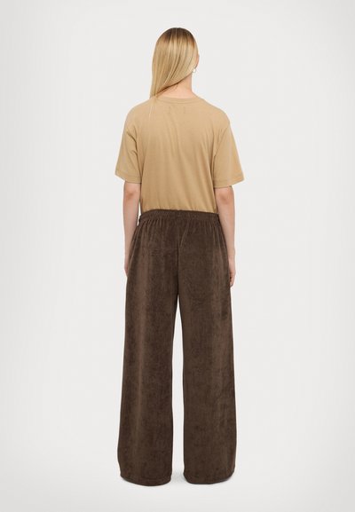 Tan katoenen t-shirt met korte mouwen, gecombineerd met brede bruine velours broeken met een elastische tailleband.