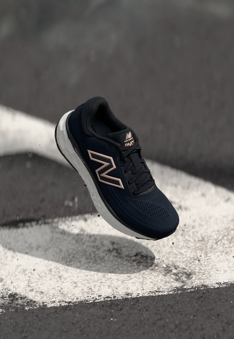 Black athletic shoe with breathable mesh upper, white midsole, and rose gold accents. Features a textured surface and lace-up design.
