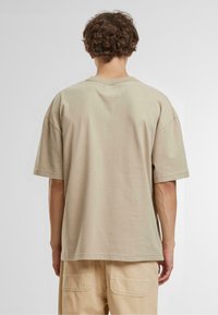 Beige, oversized pamut póló rövid ujjakkal, kerek nyakkivágással, sima textúrával és laza szabással, hátulról nézve.