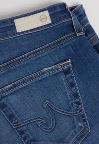 Mörkblå denimjeans med en texturerad yta. Har en läderetikett vid midjan och distinkt sömnad på bakfickan.