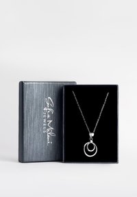 Sølvhalssmykke med dobbelt cirkulært vedhæng præsenteret i en smykkeboks med sort fløjl. Boksen har en struktureret grå yderside.