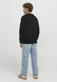 Svart bomullströja med långa ärmar, ribbade muddar och nederkant, kombinerad med ljusblå jeansbyxor och vardagsskor.