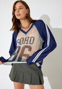 Marineblauw en kant gelaagd top met "SOHO 86" print, met witte strepenaccenten op de mouwen. Gecombineerd met een geplooide grijze rok.