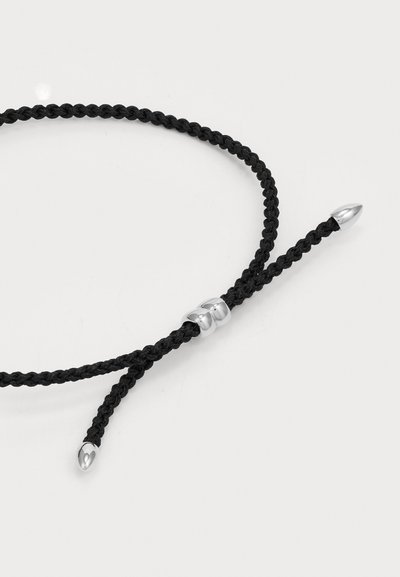Bracciale in corda intrecciata nera con accenti in metallo argentato, caratterizzato da un design elegante e estremità appuntite. Regolabile con un dettaglio a chiusura scorrevole.
