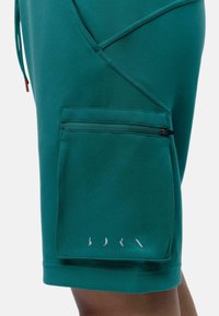 Teal sportieve shorts gemaakt van zachte stof, met een ritssluiting aan de zijkant en geometrische naaddetails. Weinig branding zichtbaar aan de zoom.