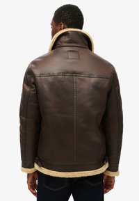 Veste en cuir marron avec un col en shearling, dotée d'une texture lisse et de sangles ajustables à l'ourlet. Conçue avec une silhouette épurée et structurée.