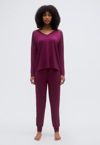 Σετ πιτζάμες μπορντό με άνετο τοπ με δαντελένιες λεπτομέρειες και στενά παντελόνια με ριμπ μανσέτες, κατασκευασμένα από απαλό, λείο ύφασμα.