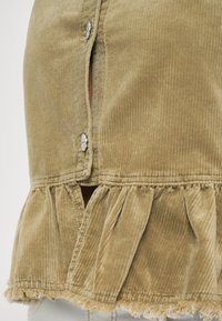 Khaki-Rippenrock mit fransigem Saum, Knopfverschluss, geflammten Akzenten und vertikal gestreifter Textur.