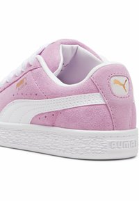 Baskets en suède rose clair avec des accents blancs, semelle blanche texturée et logo doré sur le talon. Comprend un design classique à lacets.