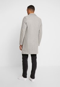 Abrigo de lana gris con cuello con muesca, cierre de un solo botón y corte entallado, combinado con jeans negros y zapatillas blancas.