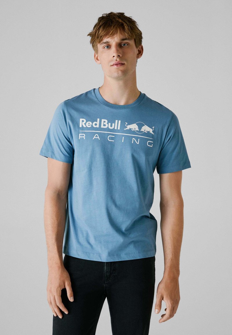 Lyseblå bomulds t-shirt med korte ærmer, der viser et hvidt trykt "Red Bull Racing" logo på tværs af brystet. Enkel, rund halsudskæring.