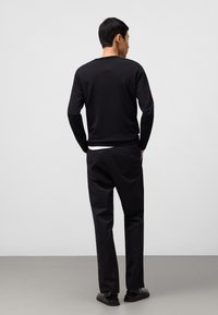 Maglietta nera a maniche lunghe con scollo rotondo, abbinata a pantaloni neri e scarpe nere. Tessuto liscio senza motivi visibili.
