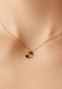 Gouden ketting met een cirkelvormige hanger met een gestructureerd zonnestraalpatroon, bevestigd aan een delicate ketting.