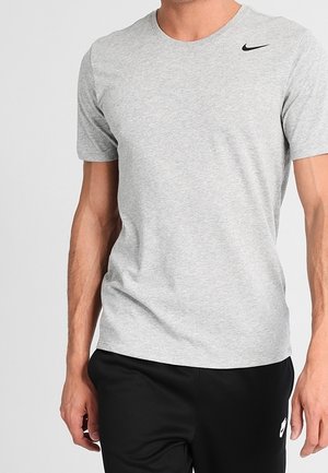 Homme portant un t-shirt Nike gris clair uni et un pantalon Nike noir, debout, les bras détendus le long du corps.