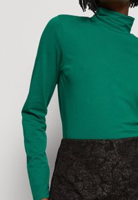 Grön långärmad polotröja i mjukt tyg, kombinerad med en strukturmönstrad svart kjol med blommönster.