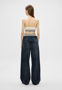 béžový crop top s tenkými ramienkami a logom, skombinovaný s voľnými tmavomodrými džínsami s prednými a zadnými vreckami a vyblednutým vzhľadom.