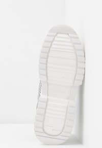 Semelle de basket blanche avec des crêtes texturées, présentant une finition lisse et un marquage subtil. Conçue avec une forme ovale et un matériau durable.