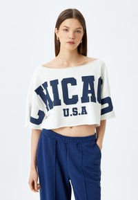 Hvid cropped sweatshirt med et stort navy "CHICAGO U.S.A." print, med rå kant og brede ærmer, parret med navy sweatsbukser.