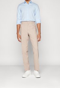 Světlomodrá košile na knoflíky s jemnou texturou, doplněná béžovými společenskými kalhotami a bílými teniskami. Kalhoty mají zúžený střih.