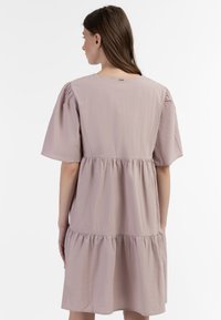 Puff-ærmeskjole i blødt mauve stof, med et lagdelt skørt og en nøglehuldetailje i ryggen. Glat tekstur; knælang silhuet.