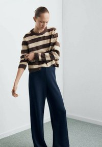 Pulover din lână în dungi maro și crem, cu croială lejeră, asortat cu pantaloni largi bleumarin. Textură netedă și design casual.