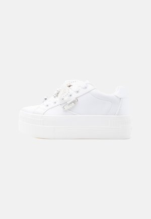 White platform sneaker with lace-up front, decorated with pearl and silver safety pin embellishments on the side and tongue.