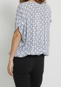Blusa dal taglio ampio bianca con motivo geometrico nero, maniche corte e scollatura arrotondata. Abbinata a pantaloni neri. Tessuto testurizzato.