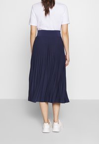 Mörkblå plisserad midikjol med hög midja, tillverkad av ett mjukt material, kombinerad med vita sneakers och en kortärmad vit T-shirt.