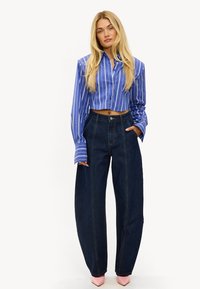 Camisa corta de rayas azules con mangas largas, combinada con jeans de mezclilla azul oscuro de talle alto, con costuras visibles y bolsillos.