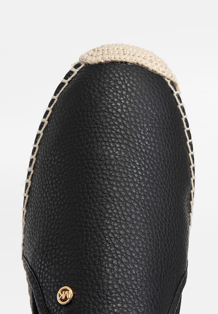 Zwarte leren schoen met een gestructureerde afwerking, voorzien van een beige geweven rand en een klein goud logo detail. Rond toedesign.