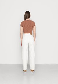 Top cropped listrado em tons de castanho e laranja, combinado com calças de cintura alta brancas e largas, apresentando um design simples nas costas e um rótulo da marca em castanho.