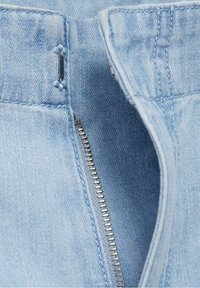 Vaaleansininen farkkukangas, jossa on metallinen vetoketju, ja siinä on ommeltu sauma sekä vyönlenkki. Vetoketju on osittain auki, paljastaen sisäosan.