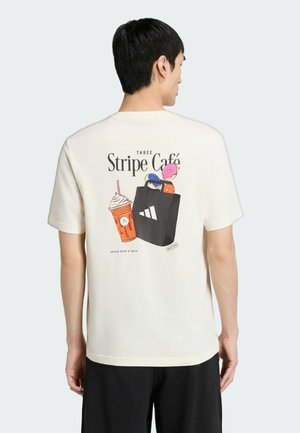 Homme portant un t-shirt blanc avec le texte « Three Stripe Café » et un dessin représentant une boisson et un sac de courses dans le dos, tourné de dos.