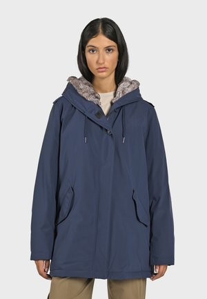 Marineblauwe jas, waterdicht materiaal, grote capuchon met nepbont voering, ritszakken en een relaxte pasvorm voor comfort.