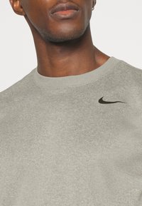 Gros plan d'une personne portant un t-shirt Nike gris clair avec le logo Swoosh noir sur le haut de la poitrine.