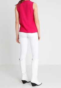 Fuchsias ärmlös topp i kombination med vita åtsittande jeans och knähöga vita stövlar med svarta klackar, som visar en slät struktur och modern skärning.